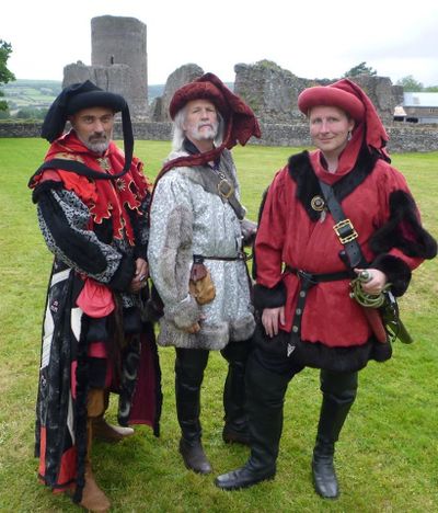 Three well-dressed Orzel nobles in chaprons. Flamboyant, bright colours, rich textiles, and an emphasis on form over function mark this as particularly Dawnish. Iconic dagging on the hood worn by the left-hand figure, andfFur trim on hems and sleeve openings to display wealth.